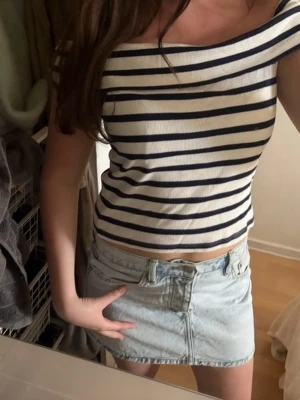 Randig offshoulder topp i bomull - Säljer en vit och marinblå randig offshoulder topp i ribbad bomull. Toppen är croppad och har en smickrande passform som sitter snyggt över axlarna. Perfekt för dig som gillar en fräsch och trendig stil.