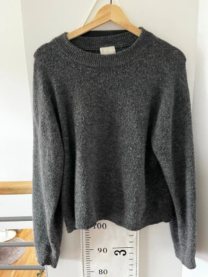 Mörkgrå stickad tröja från H&M - Mysig mörkgrå stickad tröja från H&M med rund halsringning och ribbade muddar vid ärmslut och nederkant. Perfekt för lager på lager och enkel att matcha till olika outfits. Materialet känns mjukt och behagligt mot huden.