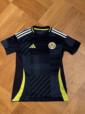 Adidas Skottland matchtröja svart/gul - Snygg matchtröja för skottska landslaget från säsongen 24/25. Köpt helt ny från JD i Skottland förra sommaren, tröjan är andvänd ett par gånger men är i väldigt fint skick, inga signs av andvändning eller missbrukande.