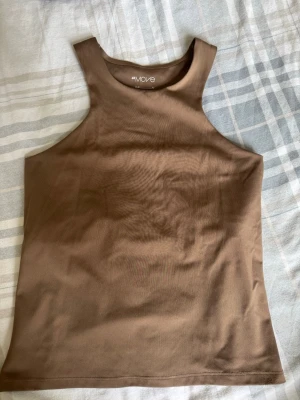 Brun ärmlös topp från H&M Move - Snygg brun ärmlös topp från H&M Move i mjukt och stretchigt material. Toppen har hög halsringning och en clean, sportig look som passar perfekt till både jeans och träningsbyxor. Enkel att styla och superbekväm.