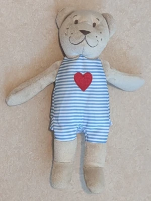 Mjukisdjur björn med randig dräkt , IKEA - Söt mjukisdjursbjörn i beige plysch med blå- och vitrandig dräkt och ett rött hjärta på bröstet. Björnen har broderat ansikte och långa armar och ben. Perfekt som gosedjur eller dekoration. IKEA märkeslapp och lappen med  tvätt instruktioner är bort klippta.