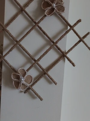 Dekorativt väggnät med jutesnöre - Säljer ett handgjort dekorativt väggnät inslaget i brunt jutesnöre, dekorerat med blommor av jute och vita pärlor samt gröna blad. Perfekt som väggdekoration eller för att hänga små lappar och foton. Säljes i set om två stycken.