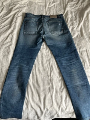 Blå tapered jeans från BOSS - Snygga blå jeans från BOSS med tapered fit och klassisk femficksdesign. Jeansen har en tvättad look med ljusare partier och kontrastsömmar. Perfekta för en avslappnad och trendig stil.