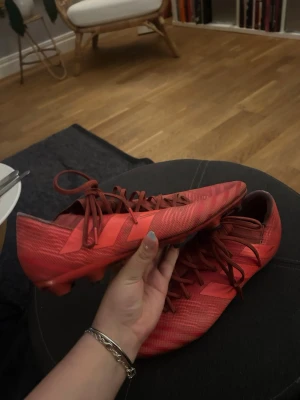 Röda fotbollsskor med snörning - Säljer ett par röda fotbollsskor med snörning och låg profil. Skorna har en modern design med mönstrad ovandel och är tillverkade i syntetmaterial. Perfekta för dig som vill sticka ut på planen med stilrena och sportiga skor.