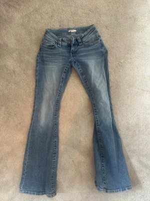 Blå bootcut jeans från Gina Tricot - Säljer ett par blå bootcut jeans från Gina Tricot i storlek 38. Jeansen har klassisk femficksmodell, låg midja och snyggt slitna detaljer framtill. Perfekta för dig som gillar en retro och avslappnad stil.