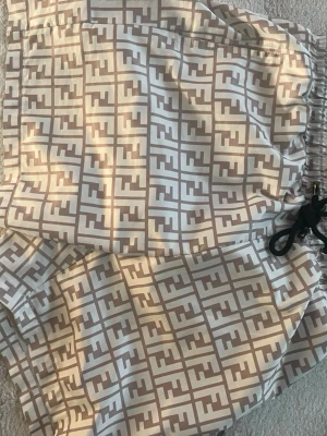 Beige och vita mönstrade shorts - Säljer ett par snygga shorts med beige och vitt rutigt mönster och elastisk midja med snörning. Shortsen har en avslappnad passform och är perfekta för varma dagar. Materialet känns lätt och luftigt.