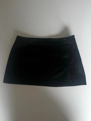 Svart satin kortkjol med slits - Snygg svart kortkjol i satin med liten slits i sidan. Kjolen har en rak passform och slät yta som ger en elegant look. 