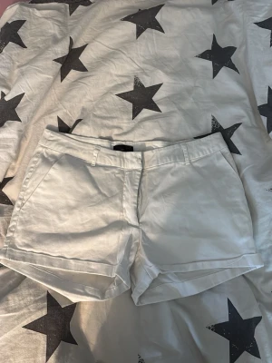 Vita klassiska shorts med fickor - Snygga vita shorts med normal passform och klassisk design. Shortsen har bälteshällor, sidofickor och är tillverkade i ett mjukt bomullsmaterial. Perfekta för varma sommardagar och enkla att matcha med olika stilar.