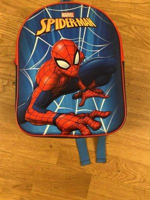 Blå Spider-Man ryggsäck Marvel - Säljer en cool blå ryggsäck med Spider-Man-motiv från Marvel. Väskan har röd kant, justerbara blå axelband och ett stort tryck av Spider-Man på framsidan med spindelnät i bakgrunden. Perfekt för dig som gillar superhjältar och vill sticka ut.