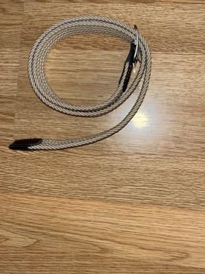 Beige flätat bälte med läderdetaljer - Snyggt beige flätat bälte med svarta läderdetaljer och silverfärgat spänne. Perfekt accessoar för att lyfta din outfit med en stilren och modern touch. Bältet har en klassisk design och passar till många olika looks.