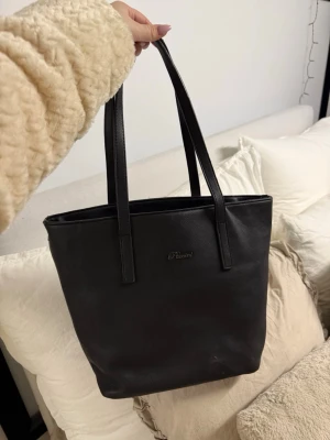 Svart handväska från puccini  - Stilren svart handväska i fejkläder med dubbla axelband och diskret logga framtill. Väskan har en rymlig insida och en praktisk dragkedjeficka på baksidan. Perfekt för dig som modern och gillar enkel design. Den är smutsig som man ser på bilden 