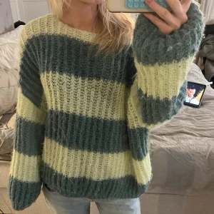 Randig stickad tröja i grönt och gult - Mysig stickad tröja med breda horisontella ränder i ljusgrönt och gulgrönt. Tröjan har en lös passform, långa ärmar och grovstickad struktur. Perfekt för dig som gillar oversized och avslappnad stil.