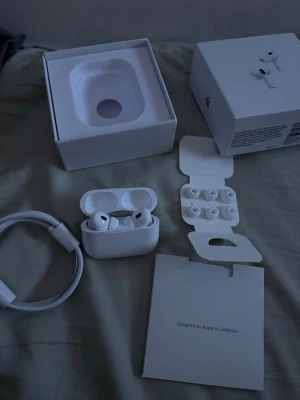 Apple AirPods Pro 2  - Säljer ett par vita Apple AirPods Pro med trådlöst laddningsetui. Hörlurarna har silikonproppar i olika storlekar, brusreducering och levereras med originalförpackning, laddningskabel och tillbehör. Snygg och stilren design i matt plast.