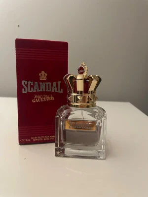Scandal Pour Homme EdT Jean Paul Gaultier - Scandal Pour Homme från Jean Paul Gaultier är en eau de toilette för män. Flaskan är fyrkantig i genomskinligt glas med en lyxig guldfärgad krona som lock. Förpackningen är djupt röd med guldiga detaljer och logotyp.50ml flaska med 35 ml kvar.