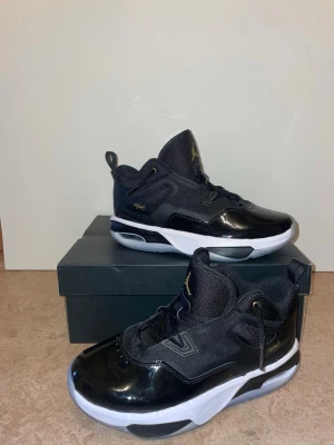 Svarta Air Jordan sneakers - Snygga svarta Air Jordan sneakers med vita sulor och gulddetaljer. Skorna har en mix av blankt och mesh-material, högre skaft och klassisk Jumpman-logga på plösen. Perfekta för dig som gillar streetwear och sportig stil.