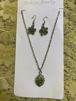 Set med halsband och örhängen, strass - Säljer två smyckeset med halsband och matchande örhängen. Ena setet har gröna och lila stenar i blommönster, det andra har röda och rosa stenar. Båda har silverfärgad kedja och krokörhängen. Perfekt för dig som gillar glittriga accessoarer. 129kr/paket /setet 