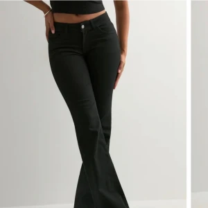 Svarta bootcut jeans med hög midja - Snygga svarta bootcut jeans med hög midja och klassiska fem fickor. Jeansen har utsvängda ben och dekorativa sömmar på bakfickorna. Tillverkade i ett stretchigt denimtyg som sitter bekvämt och formar sig efter kroppen.