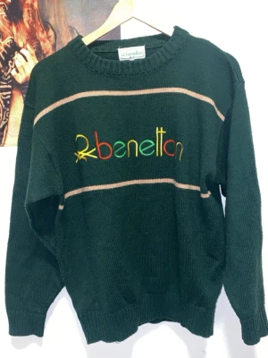 Grön stickad tröja från Benetton - United Colors of Benetton x Vintage. Mörkgrön stickad tröja med broderad logga i gult, rött och grönt framtill. Super kvalité. Priset kan diskuteras.