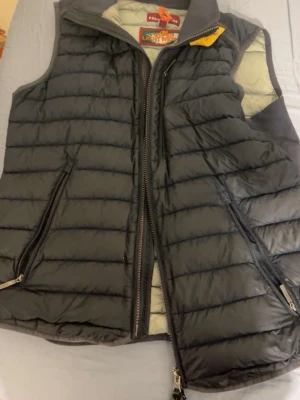 Svart dunväst från Parajumpers - Snygg svart dunväst från Parajumpers med quiltad design och två dragkedjeförsedda fickor framtill. Västen har en hög krage och gul detalj vid halsen. Perfekt för lager-på-lager och håller dig varm under kyliga dagar.