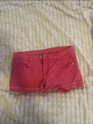 Rosa shorts från KappAhl med fransar - Snygga rosa shorts från KappAhl med råa fransade kanter nedtill och klassisk femficksdesign. Shortsen har knapp och dragkedja framtill samt bälteshällor. Perfekta för varma dagar och ger en avslappnad look.