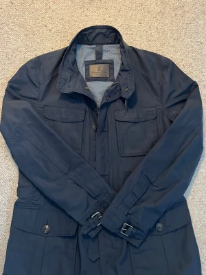Marinblå fieldjacket massimodutti  - En råklassig fieldjacket från Massimo dutti 🤩. Jackan är i fint skick och i storleken Medium, den har en marinblå exteriör kombinerat med en ljusblå interiör med vinröda detaljer, den fungerar som en riktigt bra windbraker till vår och höst och är ett perfekt plagg för den som vill ha en lit mer stilren och klassisk jacka. Kontakta mig gärna om ni önskar mer bilder, information o.s.v 🥰