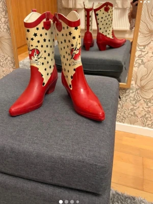 Röda cowboy boots med stjärnmönster - Unika cowboy boots i rött och vitt med svart stjärnmönster och coolt tryck med svalor och texten 'Forever'. Boots med spetsig tå, bred klack och dekorativa detaljer. Perfekta för dig som vill sticka ut! Materialet gummi..