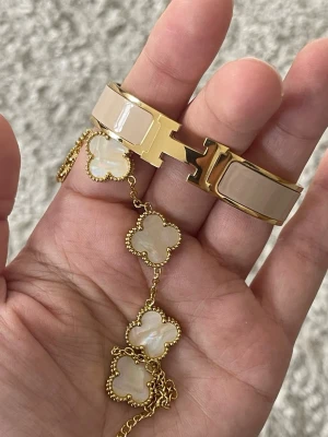 Guldigt armband med pärldetaljer - Säljer ett elegant armband i guldton med vita pärlliknande fyrklöverhängen och tunn kedja. Armbandet har fina detaljer och ger en lyxig känsla, perfekt för dig som gillar stilrena accessoarer med det lilla extra. Både armbanden för 599 fyrklöver 17+5cm andra armbandet är 16cm kolla gärna mina andra smycke och annat.