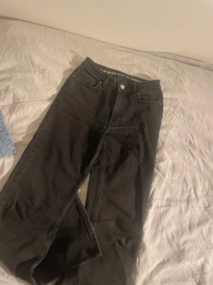 Svarta mid wide jeans med raka ben - Säljer ett par svarta jeans med mid wide passform och raka ben. Jeansen har fem fickor, knappgylf och midjehöjd. Storlek 24 i midjan och längd 30. Perfekta för en avslappnad och trendig look.