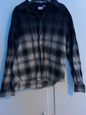 Svartvit rutig skjorta från name it - Snygg svartvit skjorta från name it med rutigt mönster och knappar framtill. Skjortan har lång ärm och klassisk krage. Perfekt för dig som gillar en avslappnad men ändå stilren look.