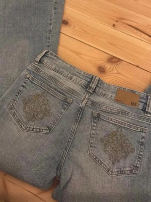Ljusblå jeans från 157 - Säljer ett par ljusblå jeans från 157 med snyggt broderade detaljer på bakfickorna. Jeansen har raka ben. De är slitna längst ner (bild finns med) 