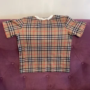 Rutig kortärmad topp från Burberry - Säljer en snygg rutig topp från Burberry i beige, svart och röd. Toppen har korta ärmar och en klassisk rund halsringning. Perfekt för en stilren look. Orginal pris. 2000kr