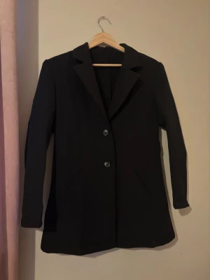 Svart klassisk kavaj med två knappar - En svart kavaj med två knappar framtill och klassisk krage. Rak passform och långa ärmar, samt två snedställda fickor. Perfekt för en stilren och enkel look. Xs i overize modell