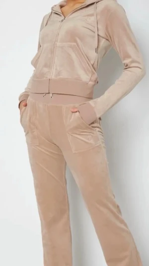 Beige velourset från Juicy Couture - Mysigt loungewear-set i beige velour från Juicy Couture. Setet består av en ziphoodie med huva, fickor och guldfärgade detaljer samt matchande byxor med dragsko och raka ben. Perfekt för chill dagar hemma eller när du vill vara extra comfy. Helt nytt skick används sällan inköp cirka 2500