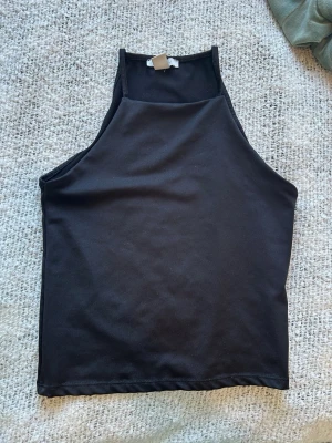 Svart ärmlös linnetopp från Amisu - Säljer en svart, stilren linnetopp från Amisu i storlek S. Toppen är ärmlös med hög hals och har en enkel, clean design som passar till det mesta. Tillverkad i mjukt material som känns skönt mot huden.