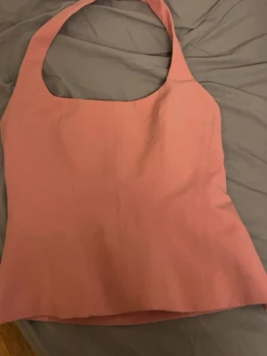 Rosa halterneck topp - Snygg rosa halterneck topp med breda axelband och figurnära passform. Toppen har en enkel, stilren design utan mönster och är perfekt för att skapa en trendig look. Materialet känns mjukt och stretchigt, vilket gör den bekväm att bära.