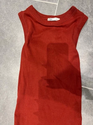 Varmröd ribbad ärmlös topp Zara - Snygg röd ribbad topp från Zara. Modellen är ärmlös med rund halsringning och har en tight passform. Perfekt att styla med jeans eller kjol för en trendig look.