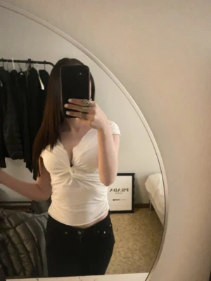 Vit v-ringad omlottopp - Snygg vit topp med v-ringning och omlottdetalj framtill. Toppen är croppad och har korta ärmar, perfekt för en trendig och stilren look. Passformen är tight och materialet känns mjukt mot huden.