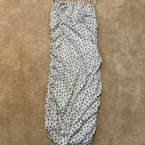 Blommig långklänning från SHEIN - Söt långklänning från SHEIN med smala axelband och blått blommönster på vit botten. Klänningen har en rak passform och är perfekt för varma dagar. Tillverkad i lätt polyester som känns skön mot huden.