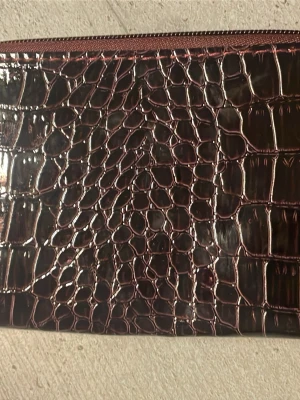 Mörkröd sminkborst necessär - Snygg mörkröd plånbok med glansig krokodilmönstrad utsida och dragkedja runtom. Insidan har flera fack för sminkborstar. Helt ny