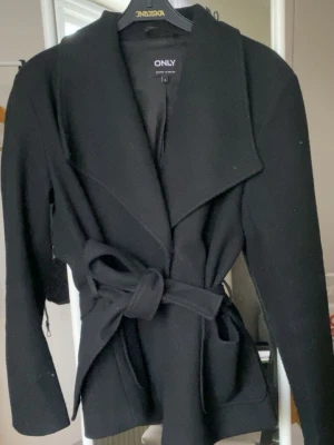 Svart kappa från ONLY - Stilren svart kappa från ONLY med bred krage och knytskärp i midjan. Köpte ny för 500.