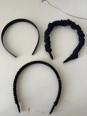 Tre svarta diadem i olika stilar - Säljer tre snygga svarta diadem: ett med tygöverdrag i skrynklig look, ett med glittrande svarta pärlor och ett enkelt plastdiadem med tänder. Perfekta för att variera din stil och hålla håret på plats.