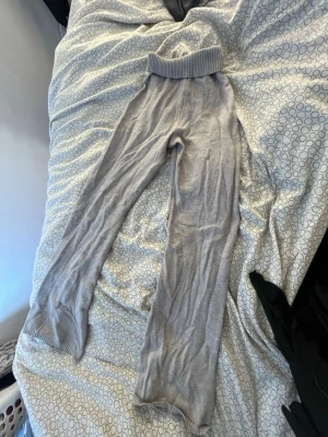 Grå ribbstickade loungebyxor + tröja  - Mysiga loungebyxor i ljusgrått med bred ribbad midja och raka ben. Byxorna är stickade i ett mjukt material som passar perfekt för chill hemma. Enkel och stilren design utan synliga fickor eller detaljer. 