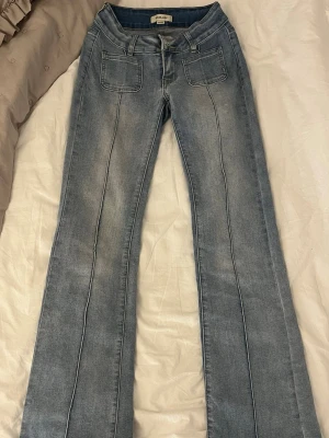 Ljusblå bootcut jeans från J.Lindeberg - Säljer ett par ljusblå bootcut jeans från Madlady med pressveck längs benen och framfickor med sömdetaljer. Jeansen har klassiska bakfickor med knapp och är tillverkade i denim med lätt tvättad look. Perfekta för en trendig och avslappnad stil.