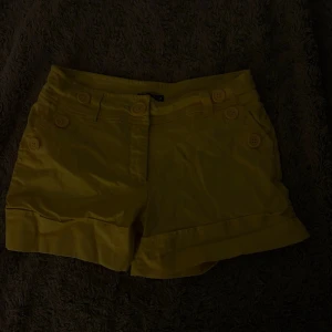 Gula shorts med knappar - Snygga unika gula shorts med dekorativa knappar framtill. Har några få små märken där fram, syns på bild 2. Vintage från Hm.