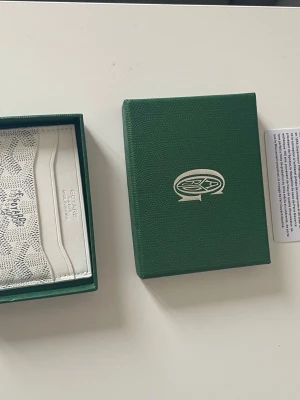 Vit korthållare - Snyggt vitt kortfodral med klassiskt mönster och flera kortfack. Tillverkat i läder med tryckt logotyp och detaljer. Kommer i original grön ask och med äkthetskort. Perfekt för dig som vill ha en stilren och exklusiv accessoar.