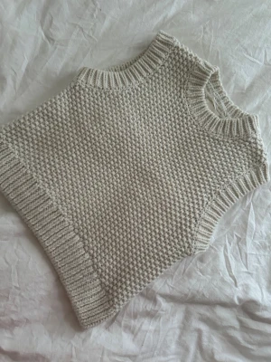 Beige stickad väst med grov struktur - Säljer en beige stickad väst med grov struktur och ribbade kanter vid hals, ärmhål och nederkant. Perfekt att styla över en skjorta eller t-shirt för en trendig lager-på-lager-look. Västen har en klassisk, rak passform och är riktigt mysig.