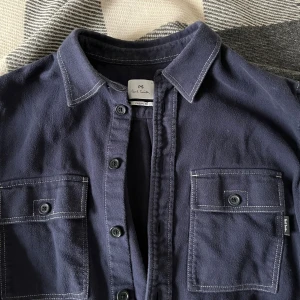 Flanellskjorta/overshirt från Paul Smith - Väldigt bra skick, tyvärr för liten för mig. Funkar jättebra som flanellskjorta men också som en overshirt. Coola sömmar. Medkommer reservknappar. Skriv vid frågor!