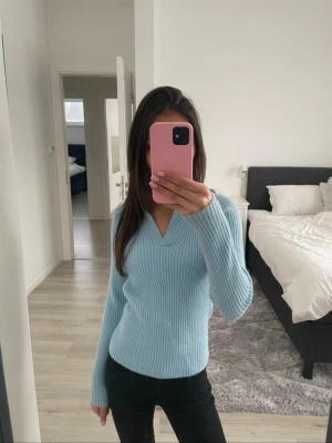 Ljusblå ribbstickad tröja - Ljusblå ribbstickad tröja med V-ringning och långa ärmar. Tröjan har en figurnära passform. Materialet ser mjukt och stretchigt ut och är väldigt bekvämt att bära.