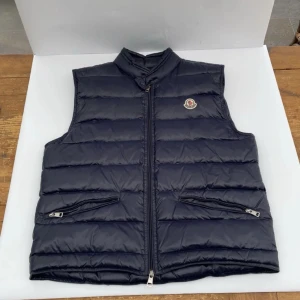 Moncler gui väst - Moncler gui väst i färgen marinblå säljs då den inte används så mycket, skick 8/10 då den har används en del men har inga skador, perfekt nu när de börjar bli lite varmare ute, passar 170cm, priset är prutbart.