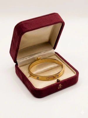 Guldigt armband med stenar - Snyggt guldigt armband i metall med infattade klara stenar och ingraverade detaljer. Armbandet har en stilren, rundad form och levereras i en elegant ask. Perfekt accessoar för att lyfta din outfit.